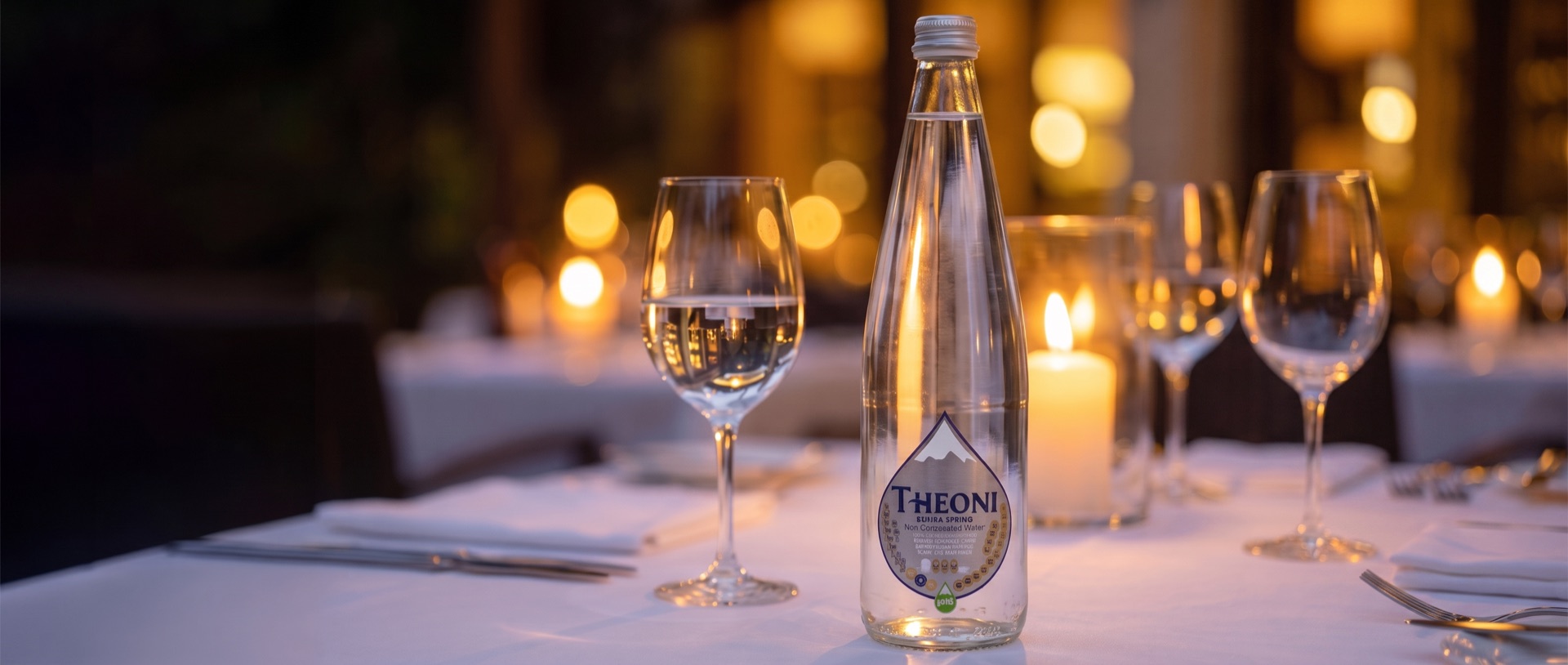 Glazen literfles THEONI op een gedekte restauranttafel bij kaarslicht